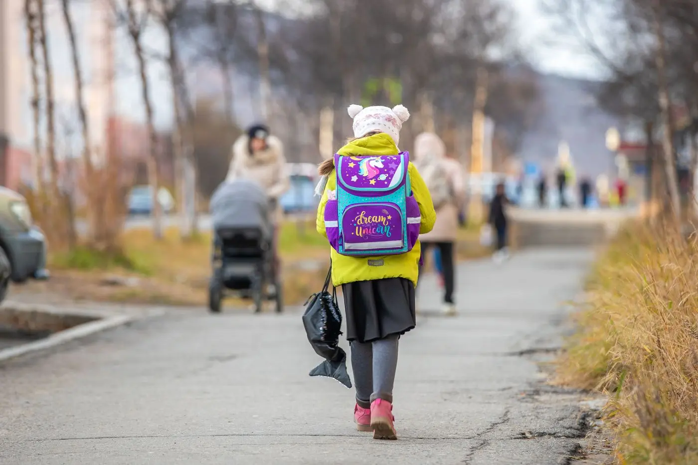 Kind met kleurrijke rugzak loopt door een herfstige straat naar school